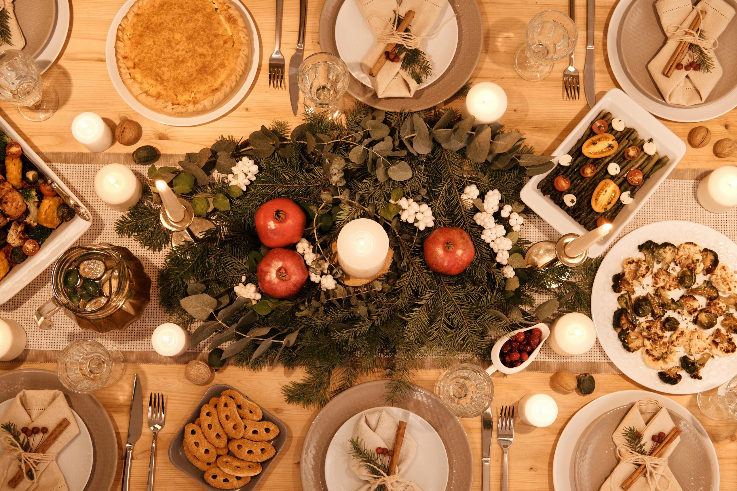 A Christmas dinner table set with plates and a centrepiece of greenery and candles, shot from overhead